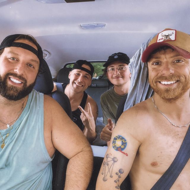 Four friends grinning in a car on a road trip