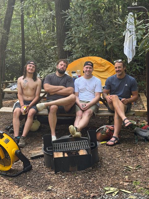Four friends at a campsite picnic table in the woods