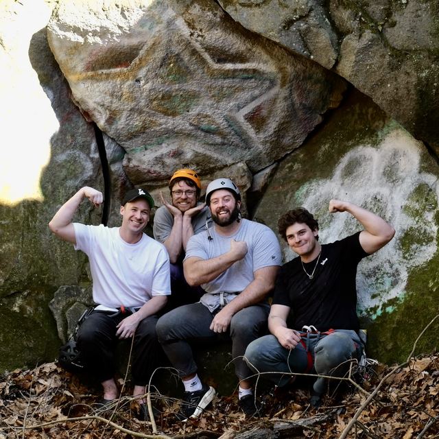 Four climbers flexing in front of a painted boulder