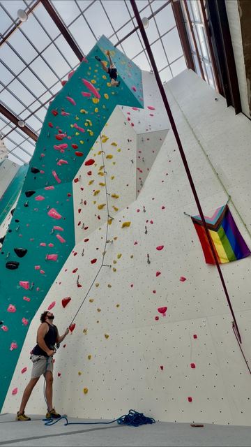 Climbing near the top of a tall indoor wall while a friend belays